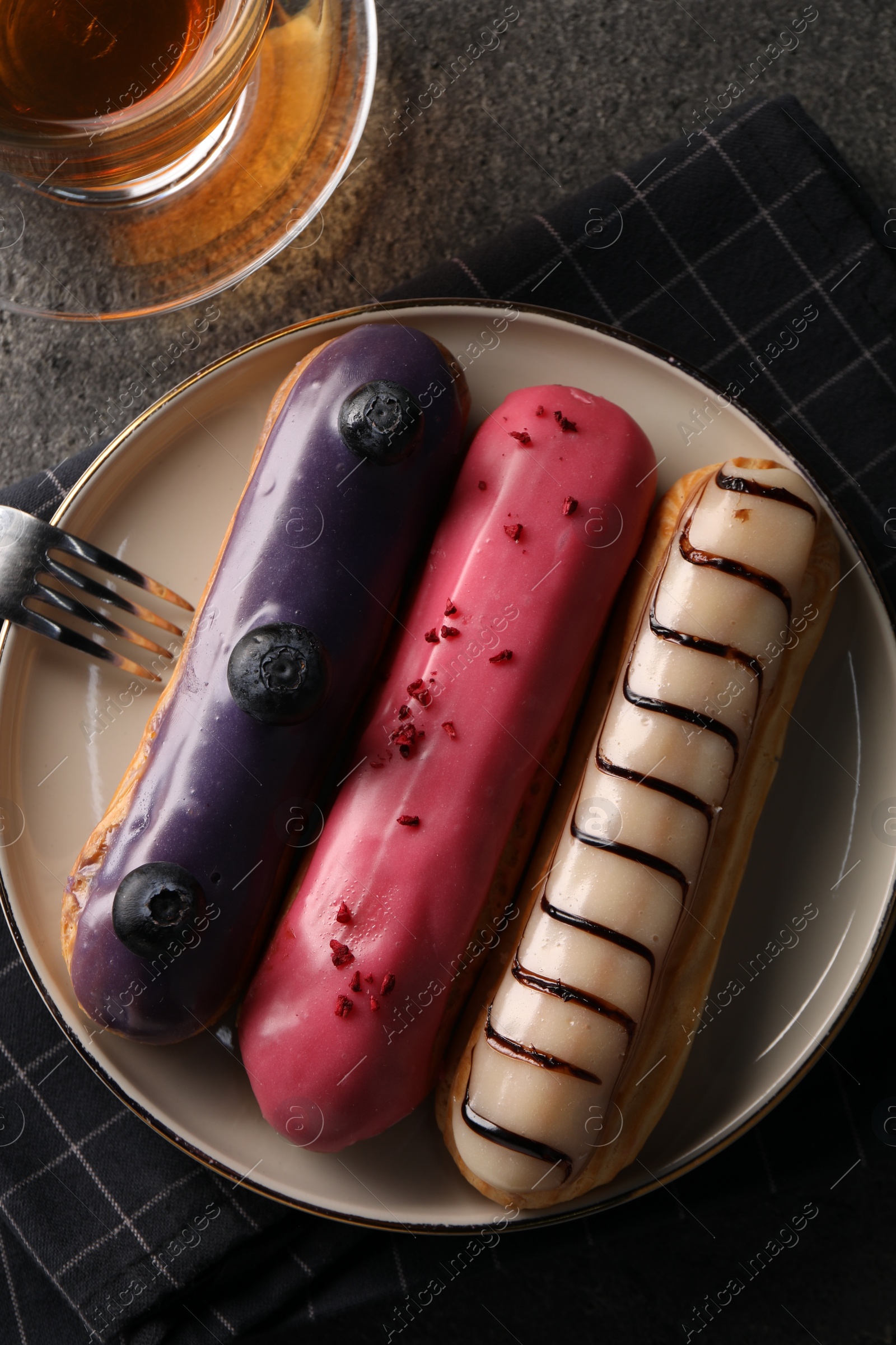 Photo of Different tasty glazed eclairs on grey textured table, top view