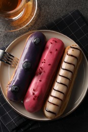 Different tasty glazed eclairs on grey textured table, top view