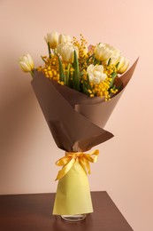 Bouquet with beautiful spring flowers on wooden table near beige wall