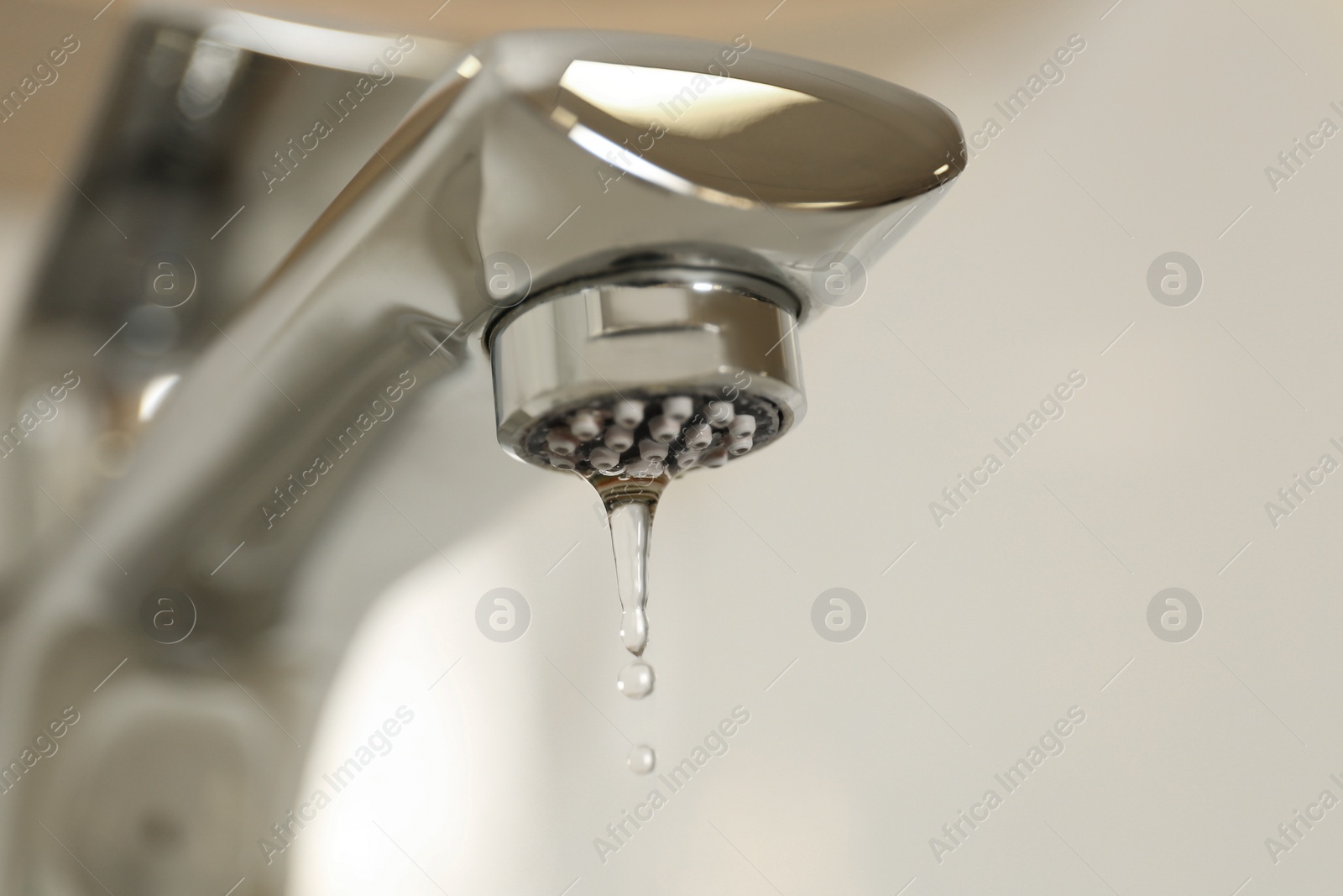 Photo of Water drops falling down from tap on light background, closeup