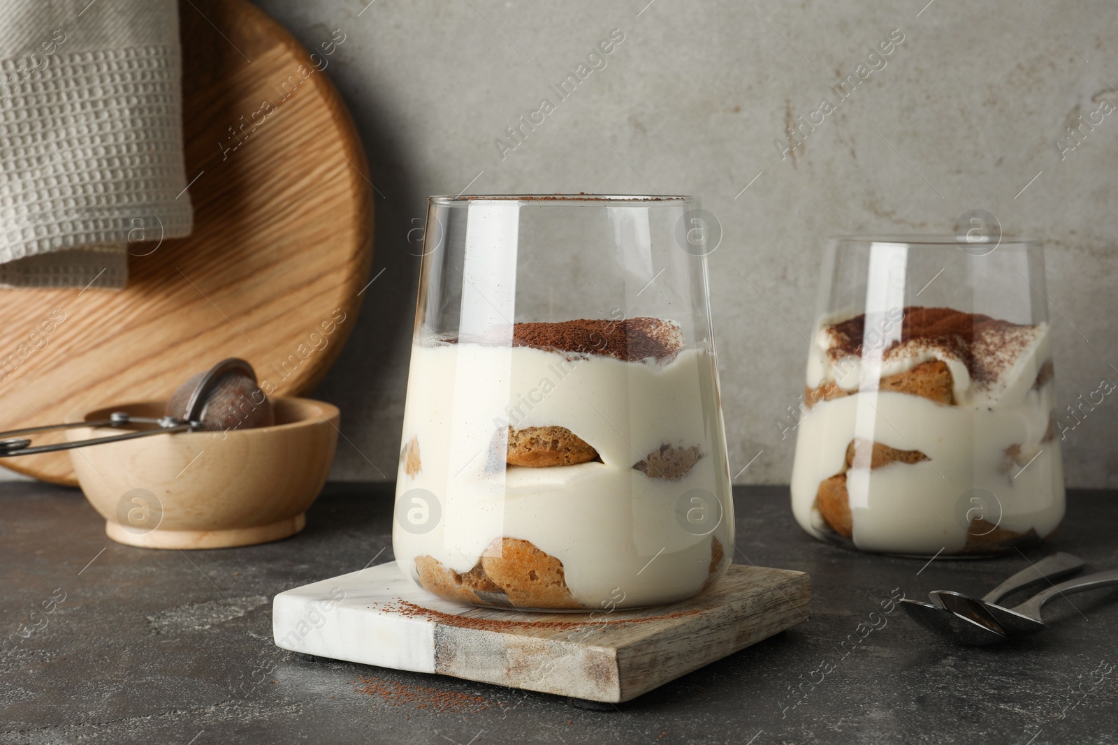 Photo of Delicious tiramisu in glasses on grey table