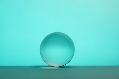 Photo of Transparent glass ball on table against turquoise background