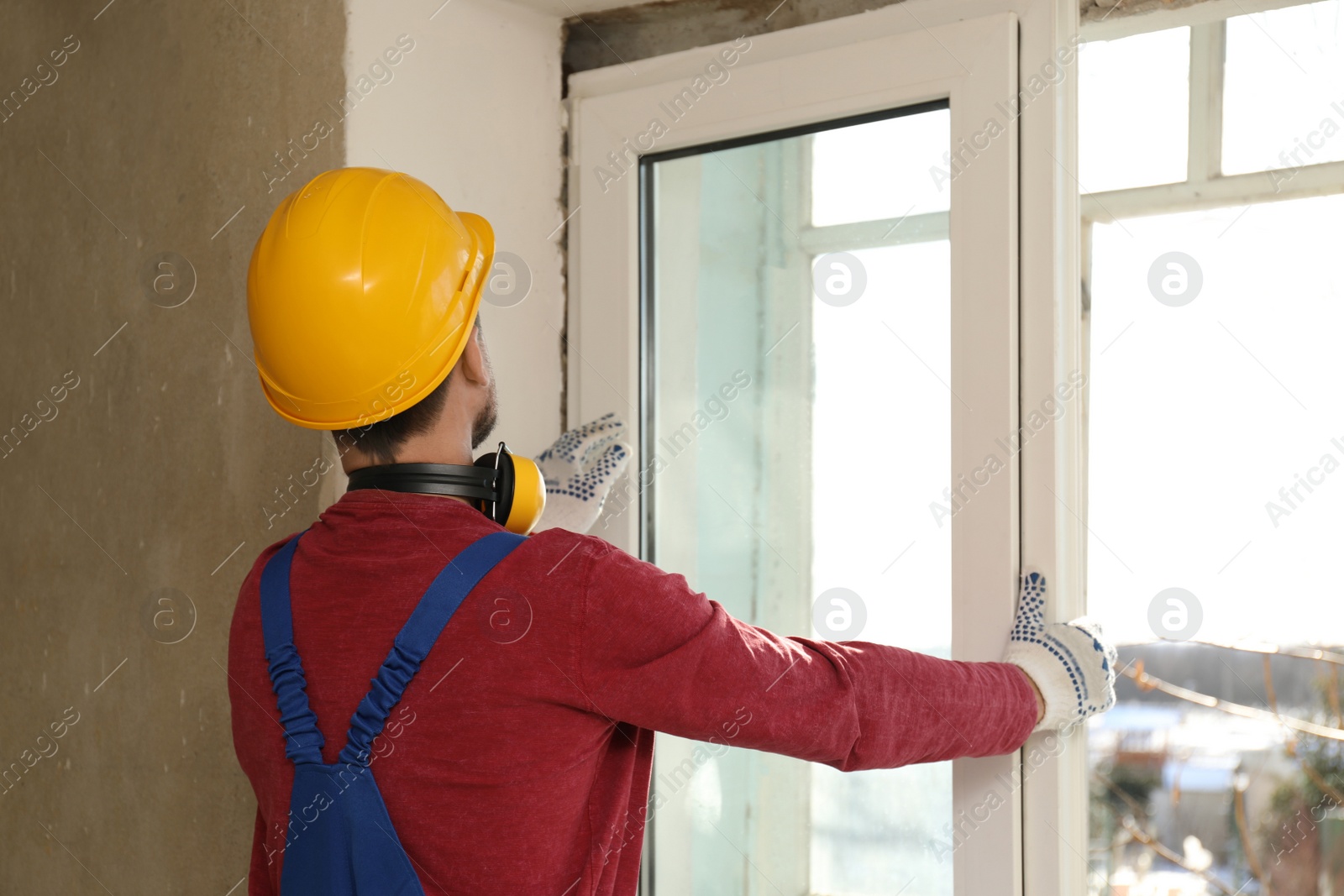 Photo of Worker in uniform installing plastic window indoors