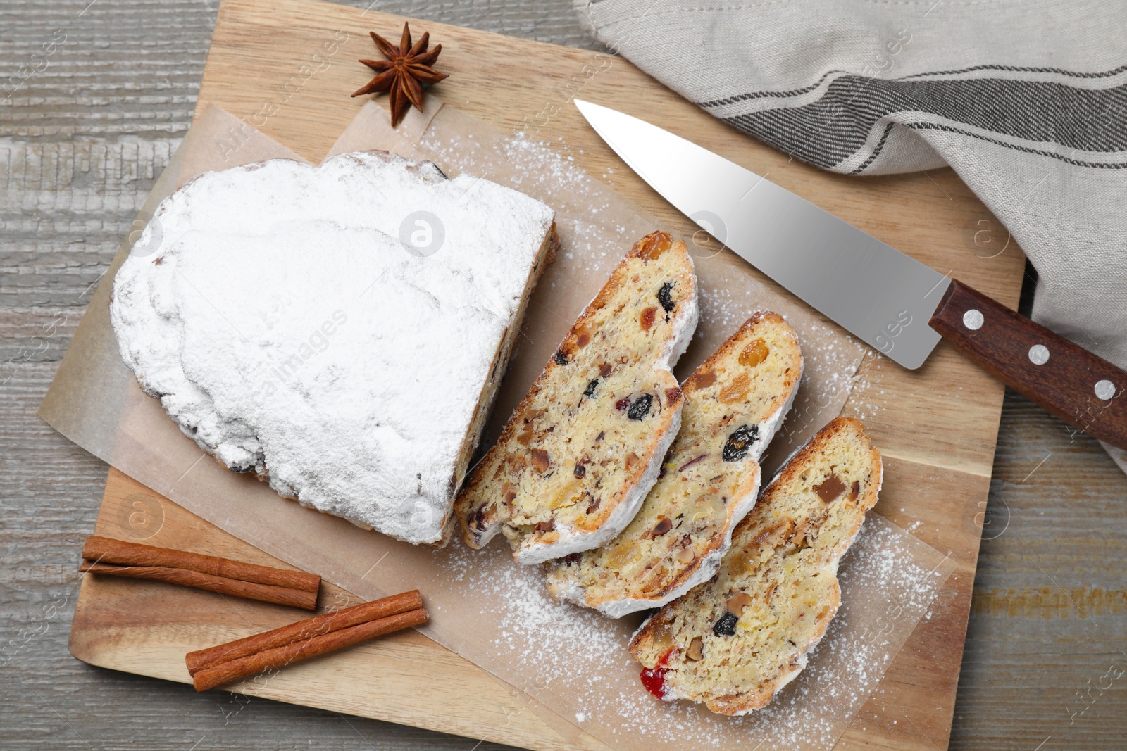 Photo of Traditional Christmas Stollen with icing sugar on wooden table, flat lay