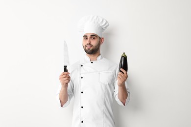 Professional chef holding knife and eggplant on white background
