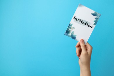 Woman holding beautiful card with word Invitation on light blue background, closeup. Space for text