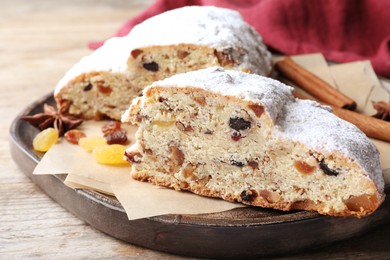 Photo of Wooden plate of cut delicious Stollen sprinkled with powdered sugar on table, closeup