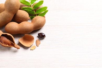 Delicious ripe tamarinds and leaves on white wooden table. Space for text