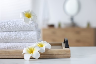 Photo of Wooden tray with stacked bath towels and beautiful flowers on white table indoors. Space for text