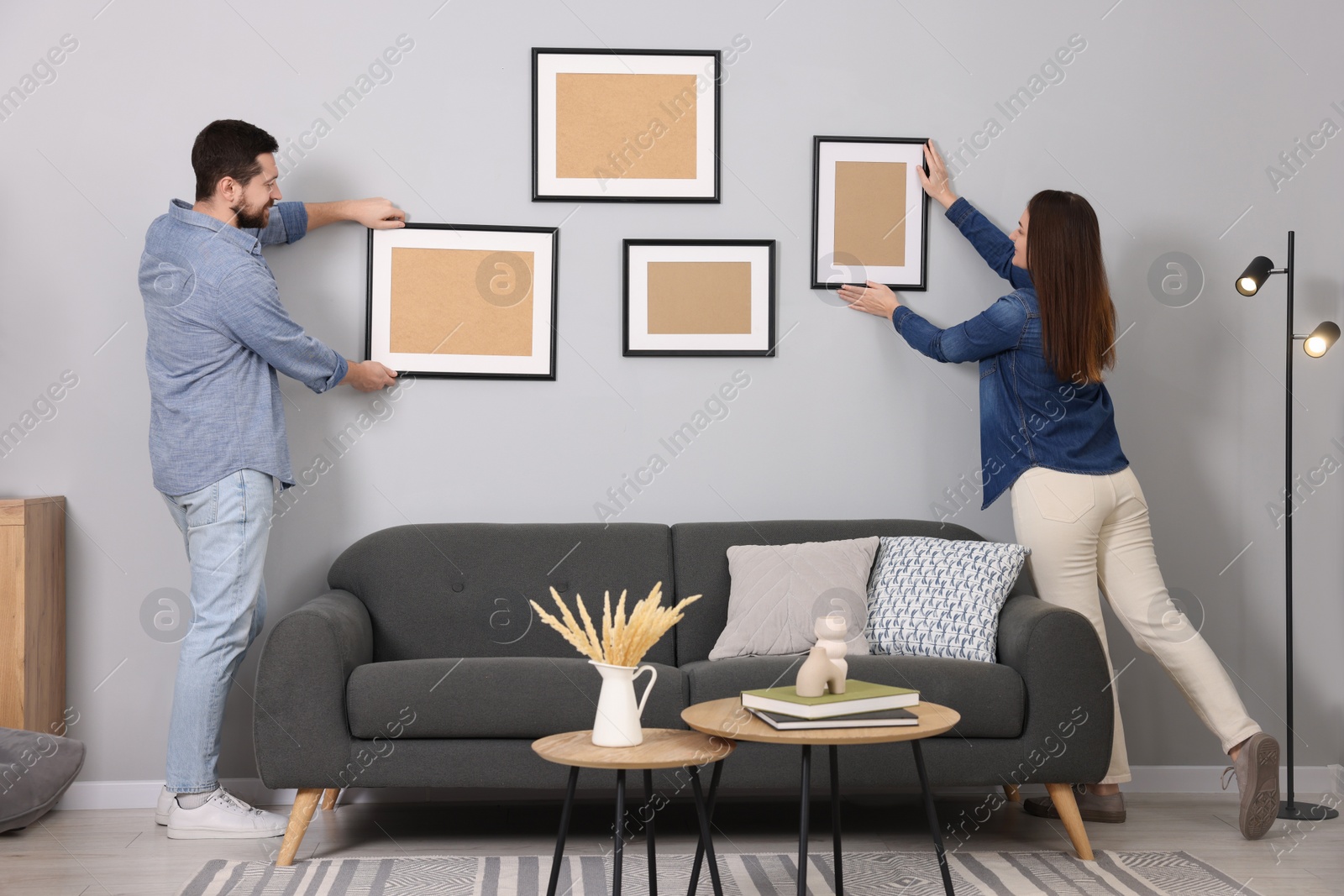 Photo of Man and woman hanging picture frames on gray wall at home