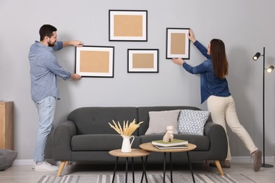 Man and woman hanging picture frames on gray wall at home