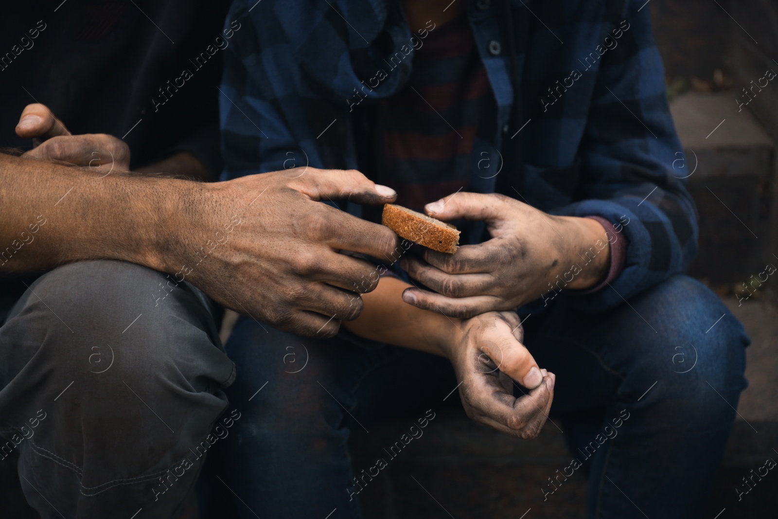 Photo of Poor homeless people sharing piece of bread outdoors, closeup