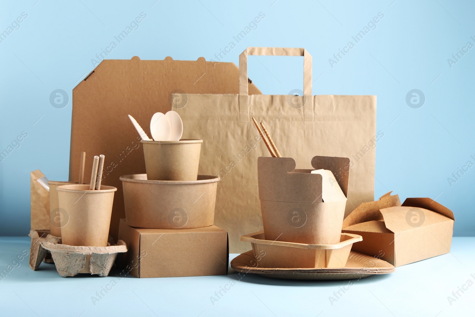 Photo of Eco friendly food packaging. Paper containers, tableware and bag on white table against light blue background