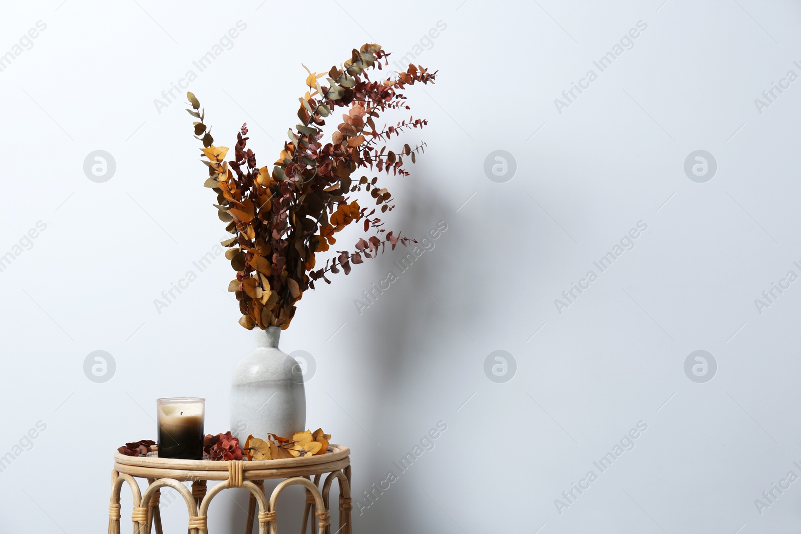 Photo of Vase with branches and candle on table near white wall, space for text