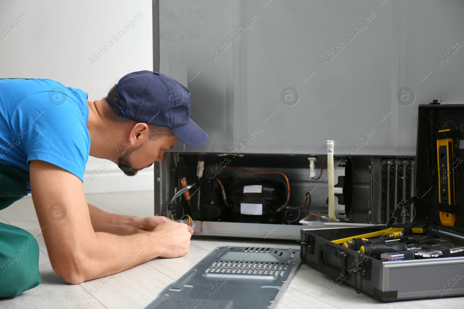 Photo of Professional male technician repairing broken refrigerator indoors