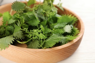 Wooden plate with fresh stinging nettle leaves on white table, closeup
