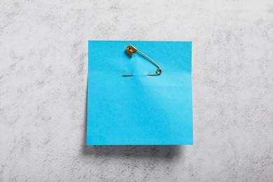 Photo of Blue paper note with safety pin on grey textured background, top view