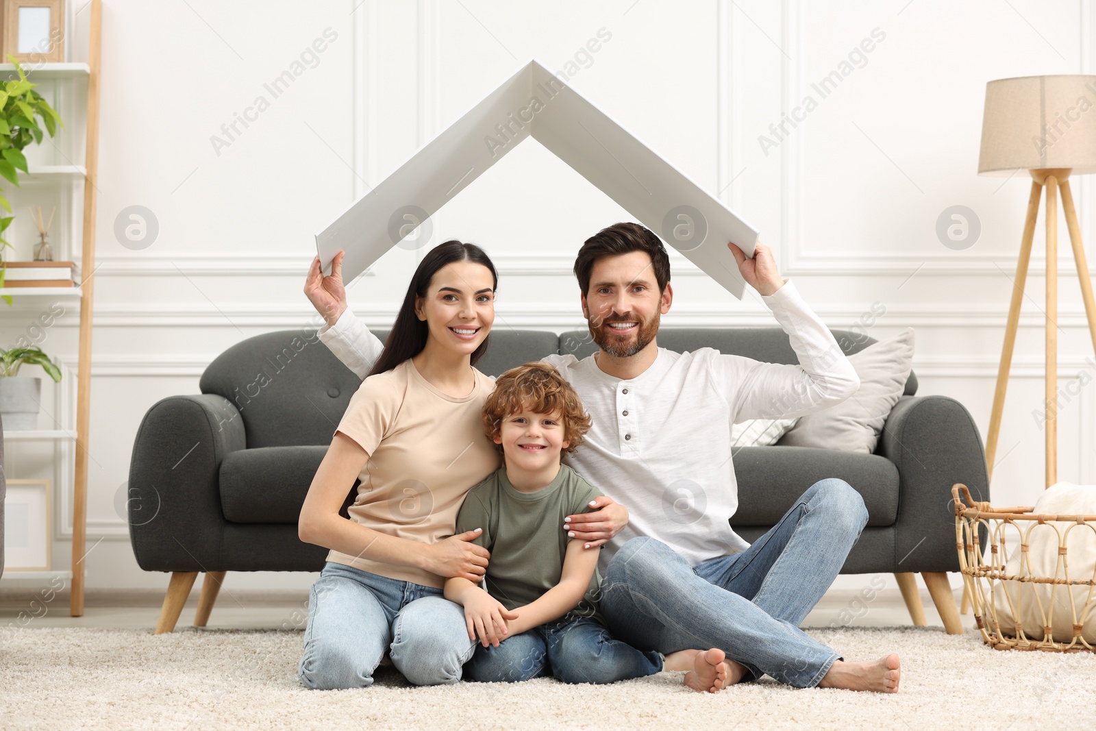 Photo of Housing concept. Happy husband holding plastic roof over his family while sitting on floor at home