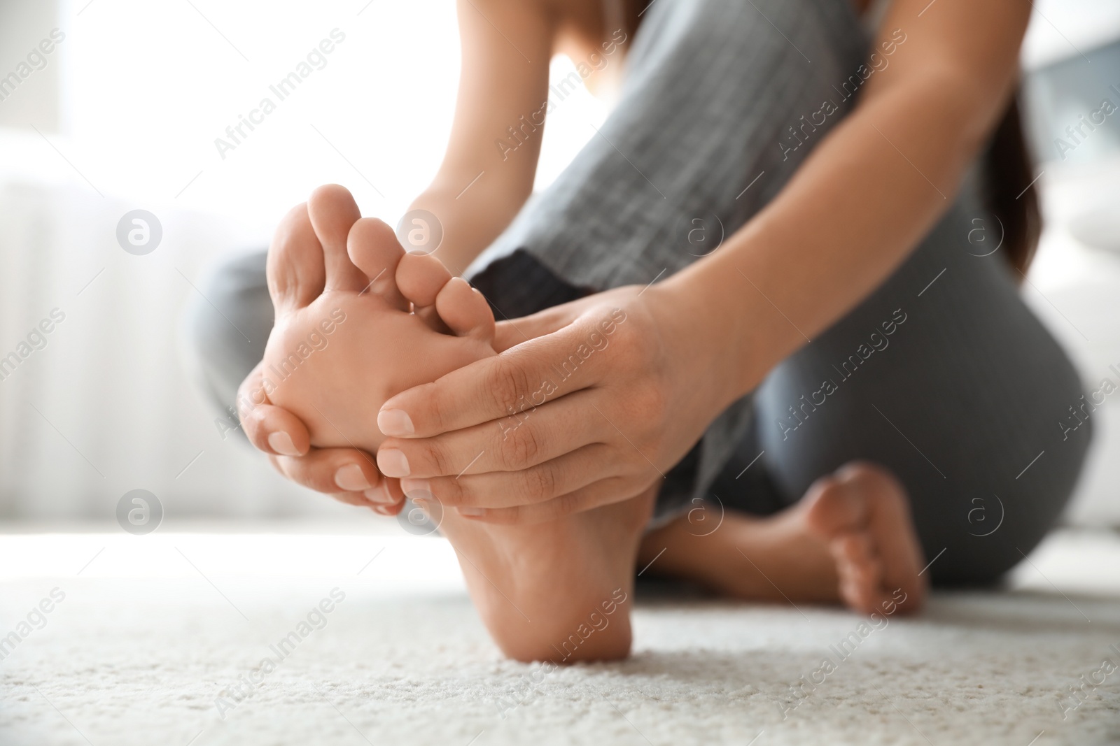 Photo of Young woman suffering from pain in foot on floor, closeup