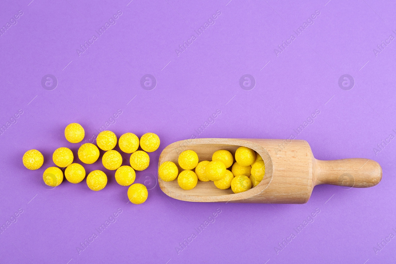 Photo of Delicious lemon chewing gums and scoop on purple background, flat lay