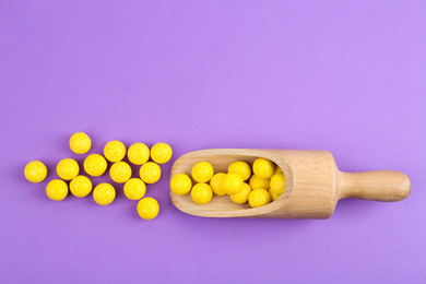 Photo of Delicious lemon chewing gums and scoop on purple background, flat lay