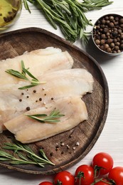 Raw cod fish, rosemary, tomatoes and spices on white wooden table, flat lay