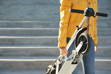 Photo of Woman carrying folded electric kick scooter outdoors, closeup. Space for text