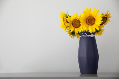 Photo of Bouquet of beautiful sunflowers in vase on table near light wall. Space for text