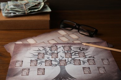 Photo of Papers with family tree templates, pencil, photos and glasses on wooden table, closeup