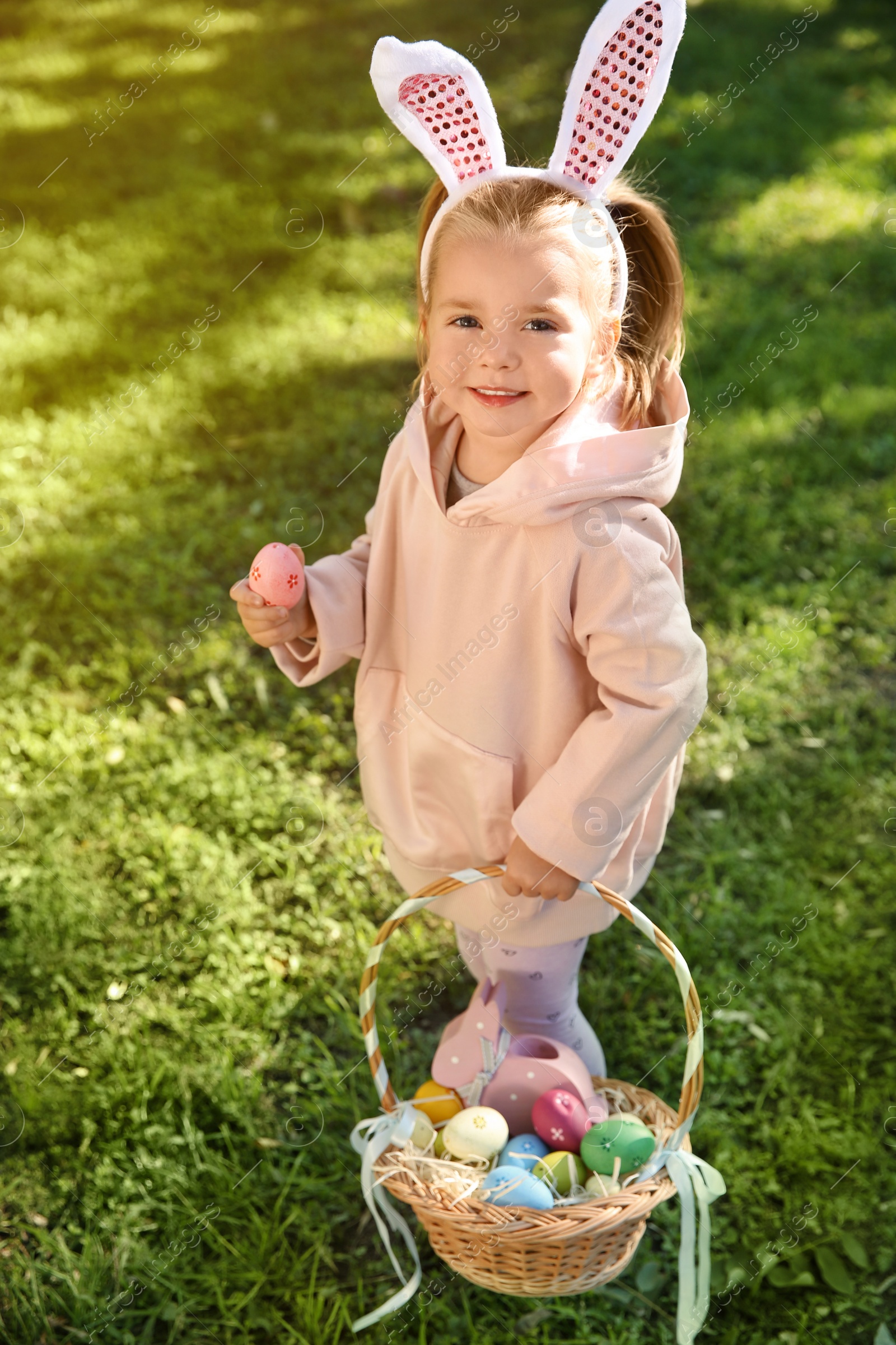 Photo of Cute little girl with bunny ears and basket of Easter eggs in park