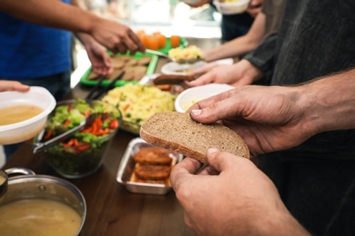 Photo of Poor man holding slice of bread at table in charity centre, closeup