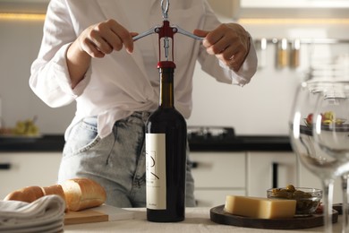 Photo of Woman opening wine bottle with corkscrew at table indoors, closeup