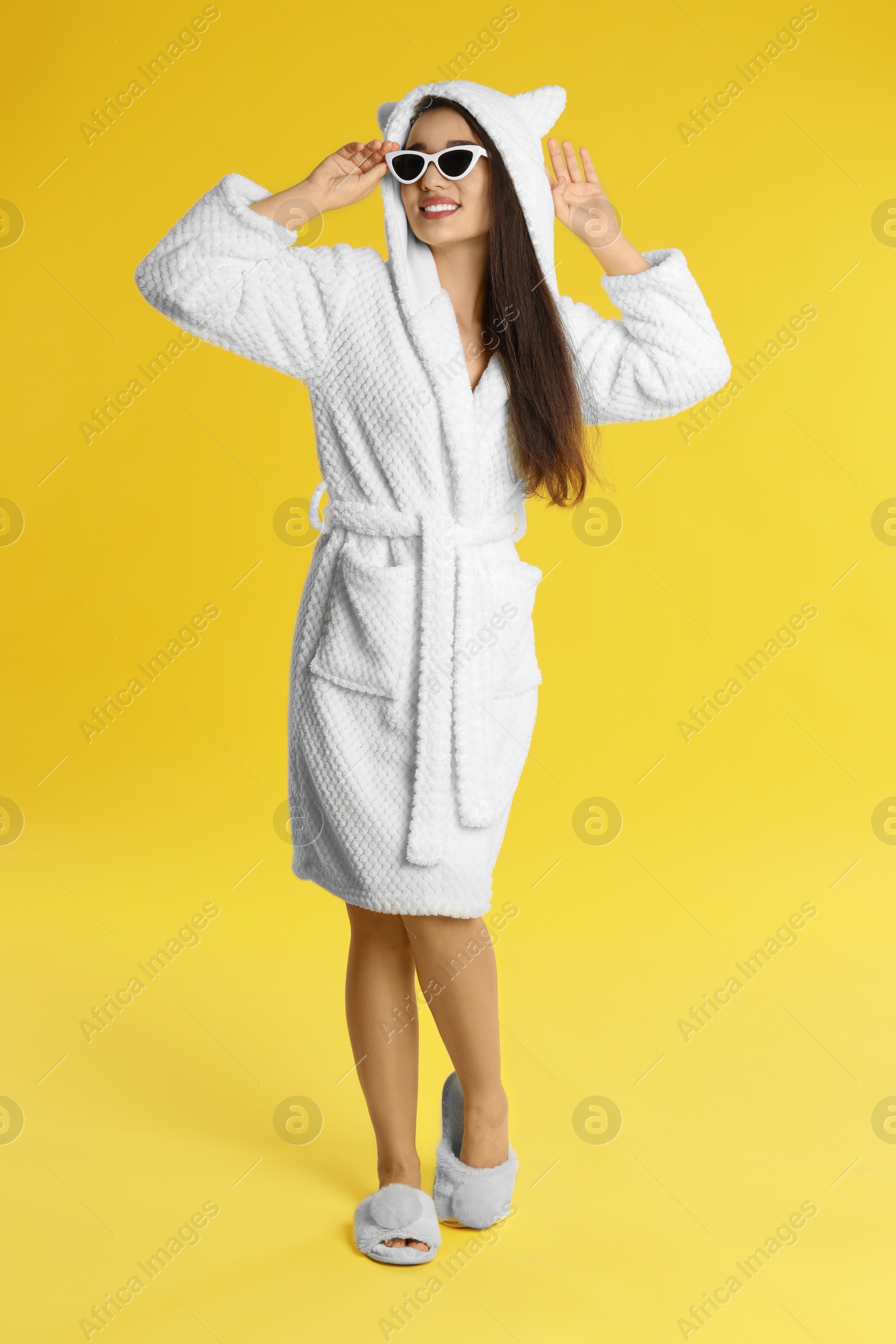 Photo of Young woman in bathrobe and sunglasses on yellow background