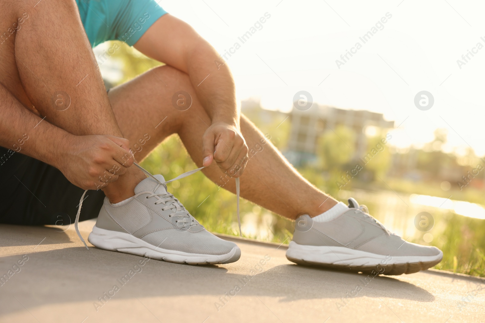 Photo of Man tying shoelaces before running outdoors on sunny day, closeup. Space for text