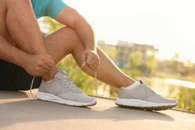 Photo of Man tying shoelaces before running outdoors on sunny day, closeup. Space for text