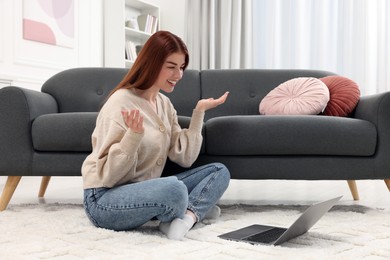 Happy woman having video chat via laptop on rug in living room