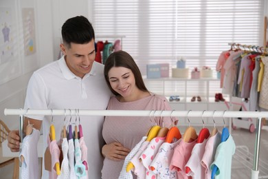Photo of Happy pregnant woman with her husband choosing baby clothes in store. Shopping concept