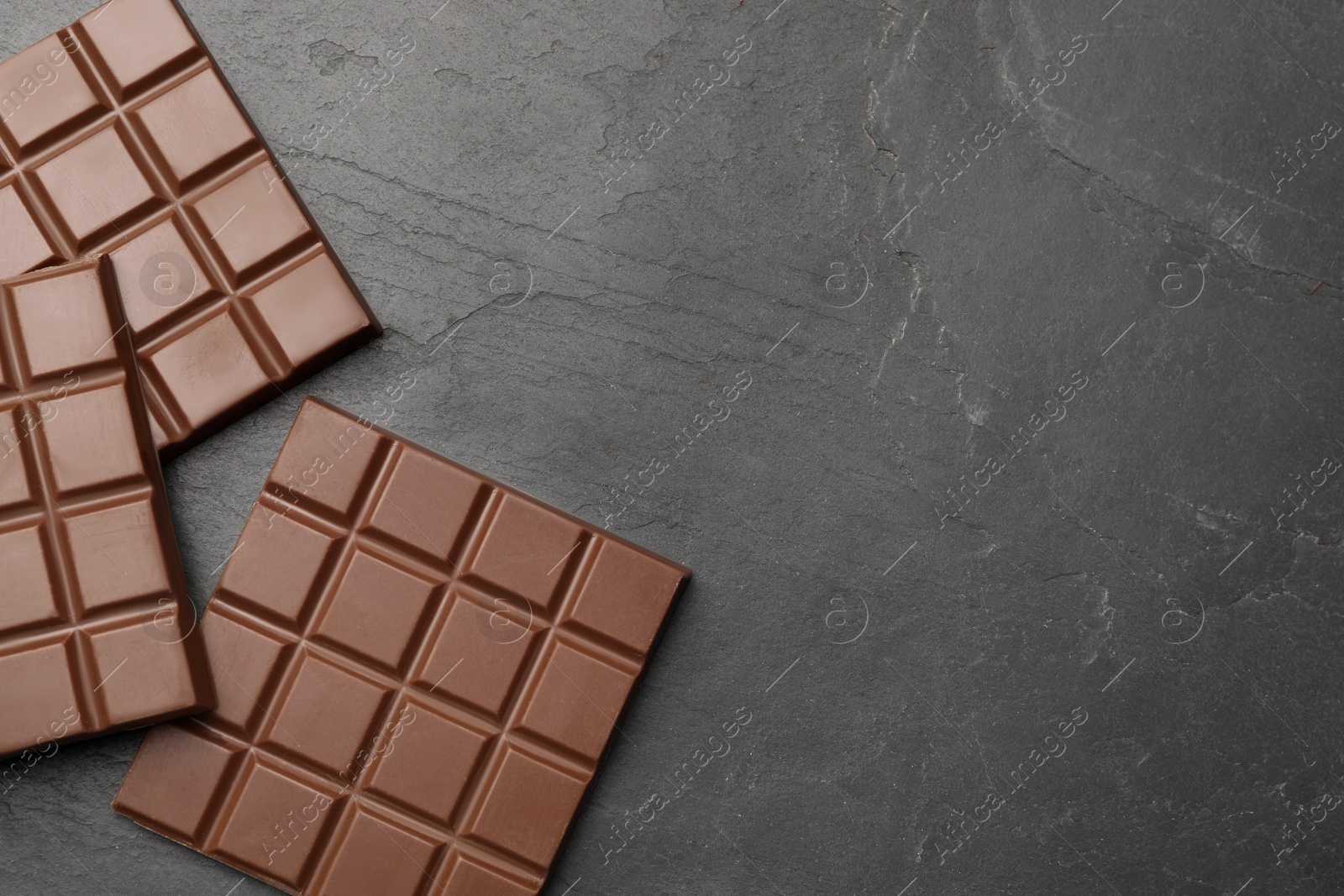 Photo of Delicious milk chocolate bars on black table, flat lay. Space for text