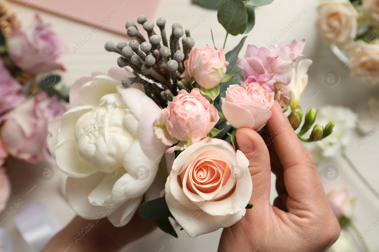 Photo of Florist creating beautiful bouquet at white table, top view