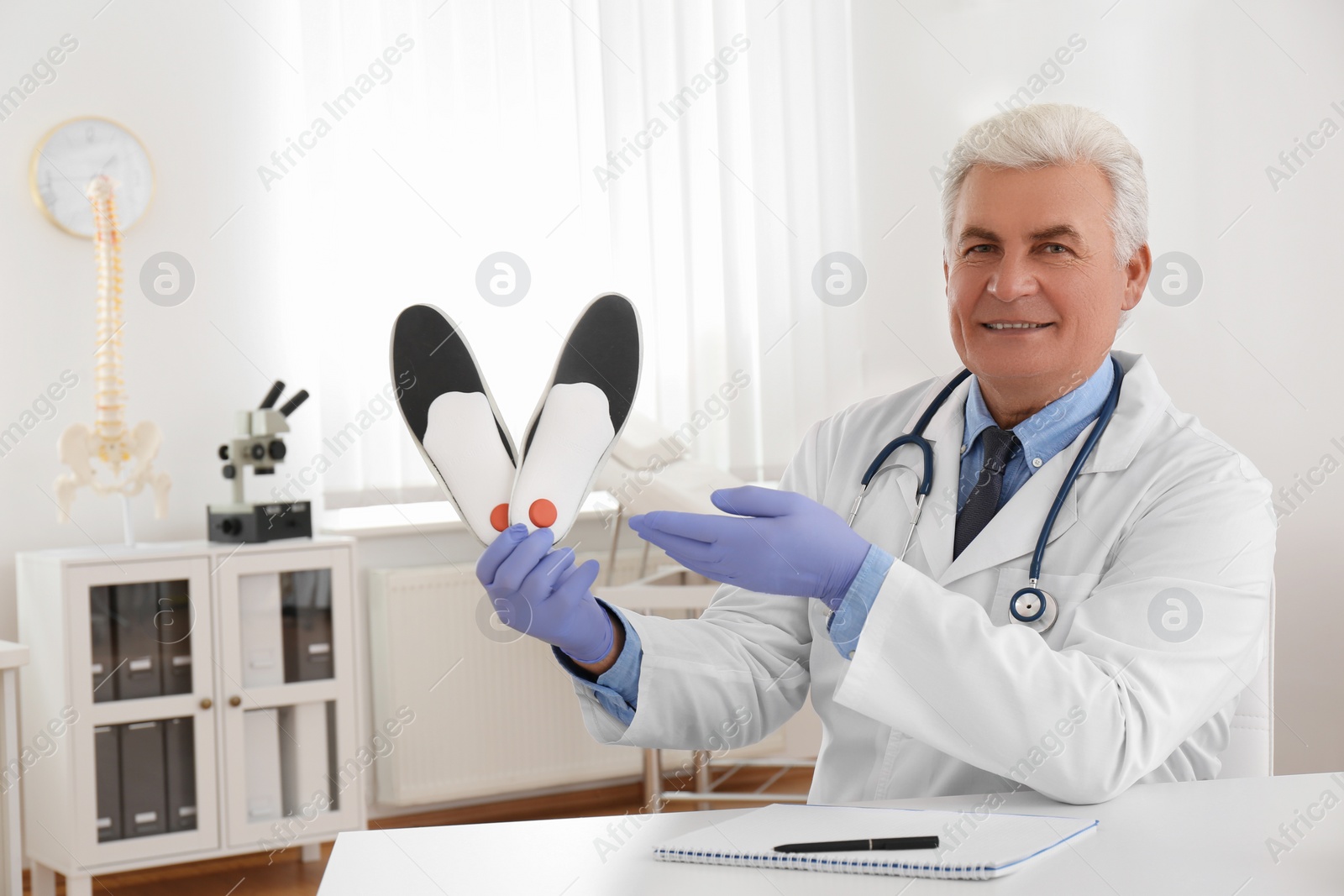 Photo of Senior male orthopedist showing insoles in clinic