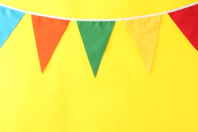 Bunting with colorful triangular flags on yellow background, space for text