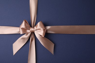 Photo of Beige satin ribbon with bow on blue background, top view