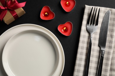 Photo of Beautiful table setting with burning candles and decorative hearts on black table for romantic dinner, flat lay