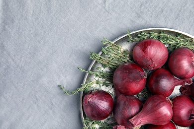 Plate with ripe red onions on fabric, top view