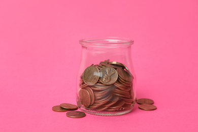 Glass jar with coins on pink background