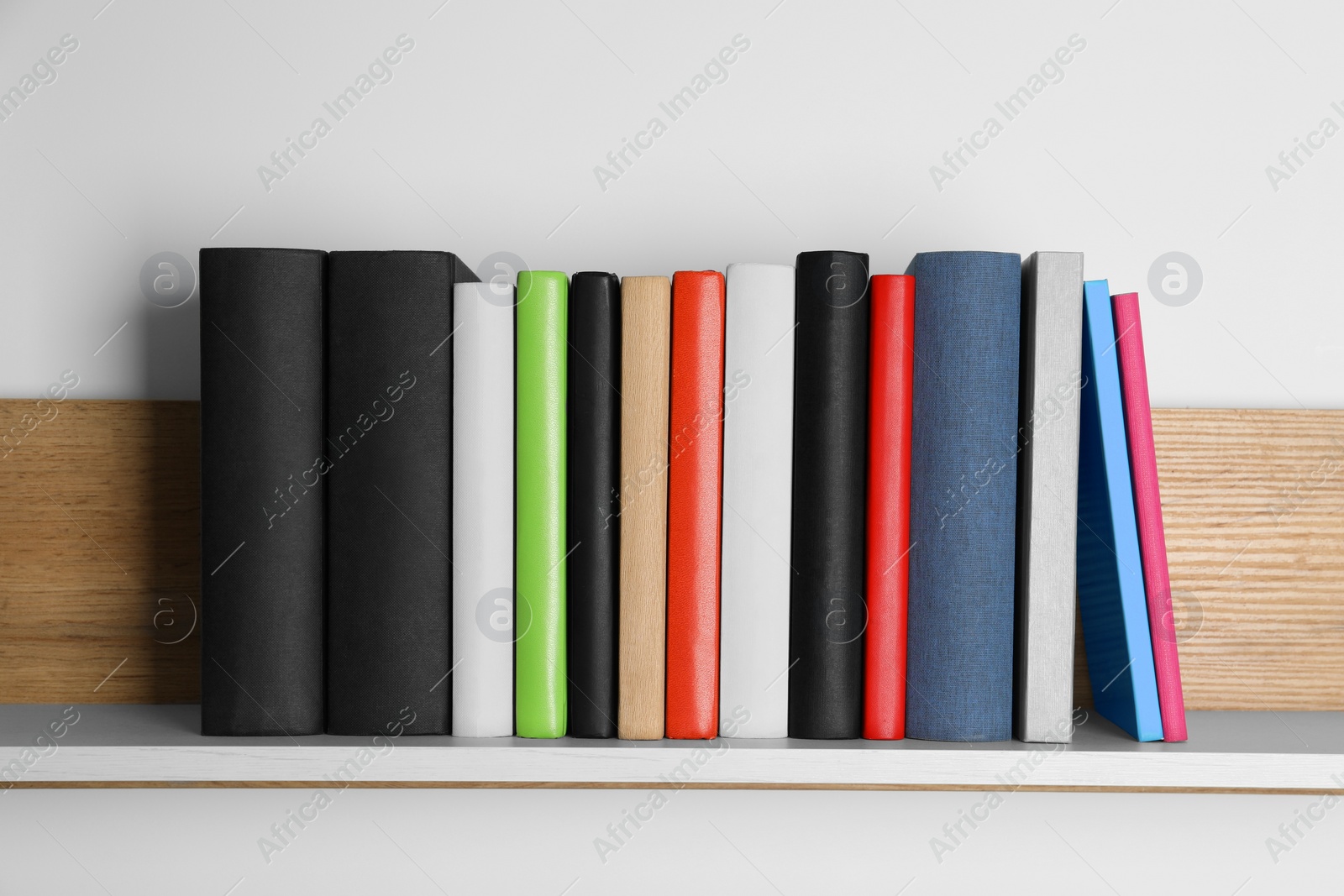 Photo of Different books on wooden shelf near white wall