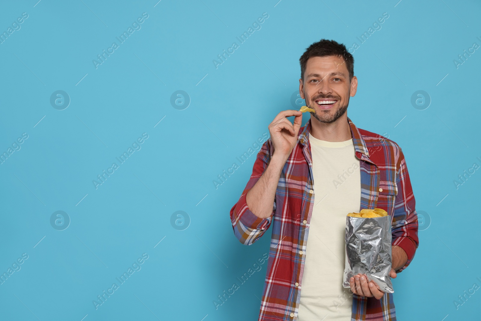 Photo of Handsome man eating potato chips on light blue background, space for text