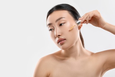 Photo of Beautiful young woman applying cosmetic serum onto her face on white background, space for text
