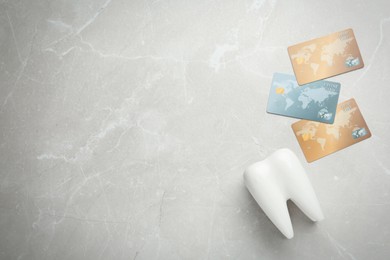 Photo of Ceramic model of tooth and credit cards on light grey table, flat lay with space for text. Expensive treatment