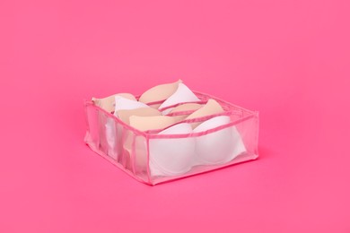 Photo of Transparent organizer with bras on pink background